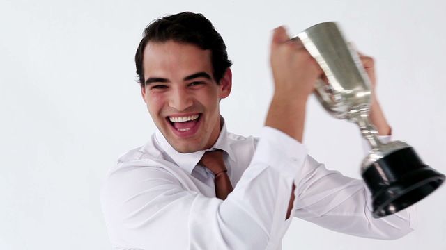 This video depicts a smiling businessman holding a trophy against a white background, exemplifying corporate success and achievement. It is ideal for use in materials related to business awards, career accomplishments, motivational content, corporate events, and advertising campaigns focusing on professional success.