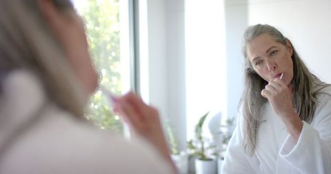 Mature Woman Applying Makeup Thoughtfully in Mirror