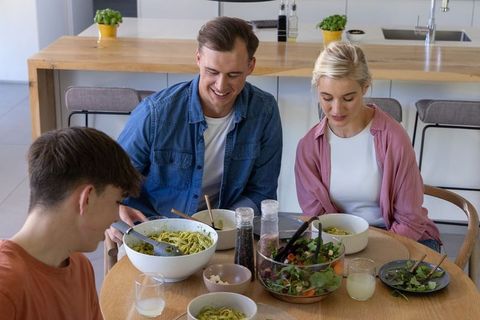 Family sharing relaxed pasta dinner and fresh salad at modern wooden dining table