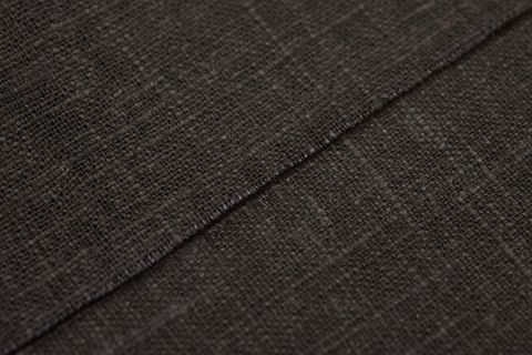 Black linen fabric close-up showing diagonal seam, woven texture and subtle fibers
