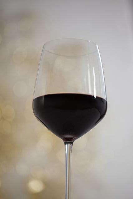 This image captures a close-up of a red wine glass with a defocused, festive background, ideal for use in holiday-themed promotions, advertisements for wine or fine dining, and celebratory event invitations. The elegant and sophisticated feel makes it suitable for luxury brand marketing and festive greeting cards.
