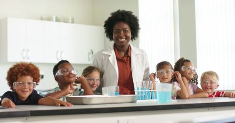 African american teacher leading kids doing hands-on science with test tubes and safety goggles