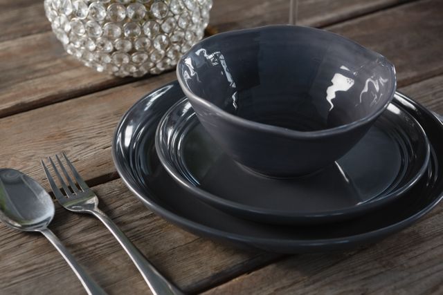 This image showcases elegant black crockery and cutlery arranged on a rustic wooden table. Ideal for use in articles or advertisements related to dining, home decor, kitchenware, and modern table settings. Perfect for illustrating stylish and contemporary dining experiences.