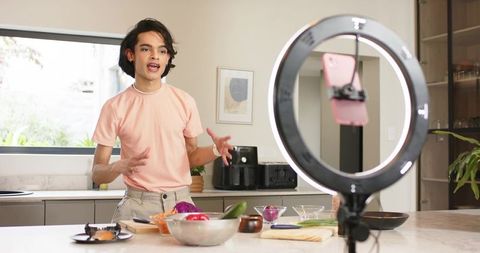 Young content creator filming cooking tutorial at modern kitchen island with ring light