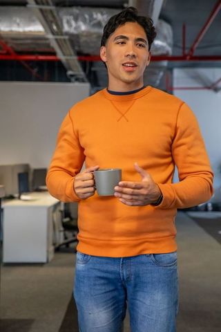 Young asian professional speaking and holding coffee mug in modern open office workspace