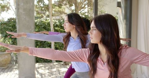 Women Embracing Warrior II Pose Outdoors on Wooden Deck