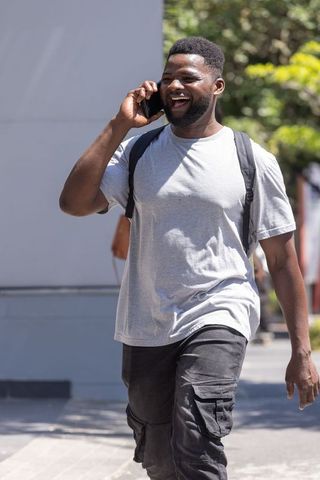 African american man walking and talking on smartphone wearing backpack in sunny city