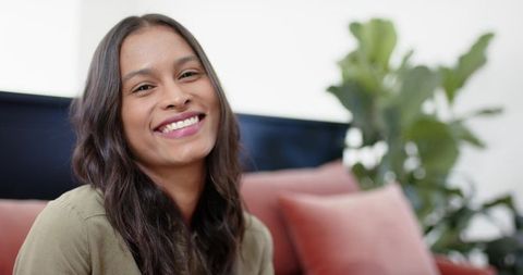 Smiling woman relaxing on rust sofa with indoor plant natural light lifestyle portrait