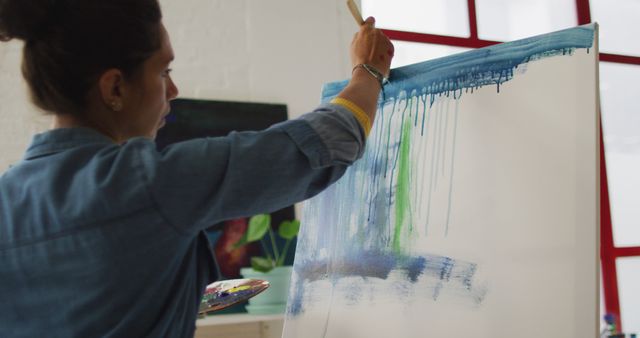 Woman painting an abstract piece on a large canvas in a well-lit art studio. Ideal for projects related to creativity, art education, and inspirational content.