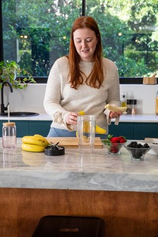 Woman preparing smoothie with fresh fruit in modern kitchen