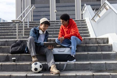 Diverse male students sitting on urban campus steps studying on tablet and sharing ideas