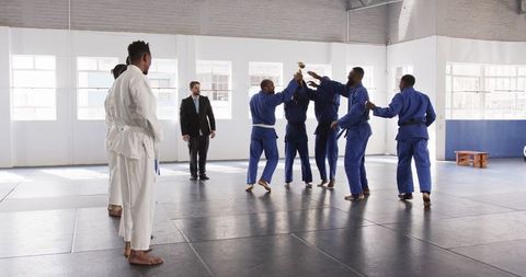 Diverse judo team celebrates victory with trophy in dojo