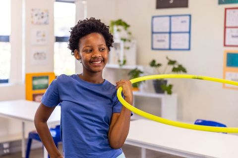 African american girl holding yellow hula hoop smiling in elementary classroom