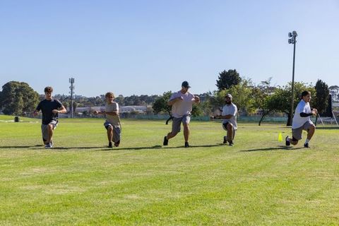 Diverse male athletes performing coordinated lunges on grass field during outdoor training