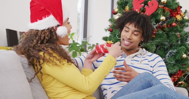 Image of happy diverse couple exchanging christmas gift and embracing at home - Download Free Stock Photos Pikwizard.com
