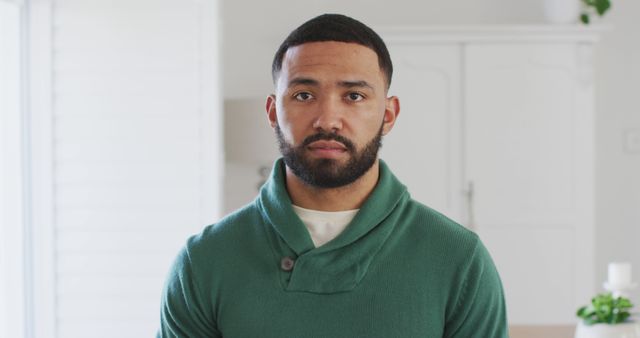 Young man standing indoors wearing green sweater, looking confident. Useful for lifestyle content, clothing advertisements, personal development materials, and modern living concepts.