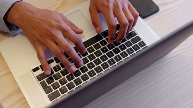 Close-up of a businessman using a laptop in a modern office. The hands on the keyboard suggest productivity, technology, and a professional environment. Perfect for illustrating business, remote work, office productivity, and technology-related themes.