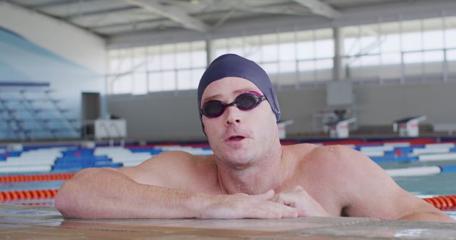 Portrait of caucasian male swimmer in cap and goggles at the side in indoor pool. Competition, training, fitness, exercise, healthy lifestyle, sport, swimming and swimming pool,
