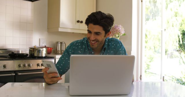 Smiling Man Working on Laptop and Using Smartphone in Kitchen - Download Free Stock Images Pikwizard.com