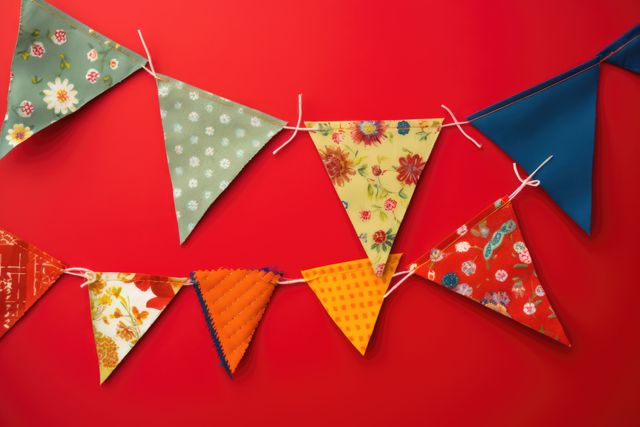 Colorful bunting flags hang against a vivid red background, creating a bright and cheerful decor. Ideal for usage in promotions for celebrations, parties, festivities, and DIY decoration inspirations.