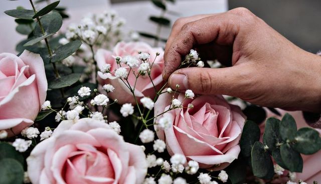 Florist hand adjusting baby's breath in pale pink rose bouquet with eucalyptus