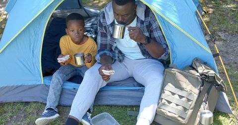 African american father and son camping morning coffee and sandwiches at blue tent