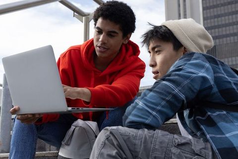 Multiracial Teens Collaborating on Laptop on Urban Steps Studying Together for School