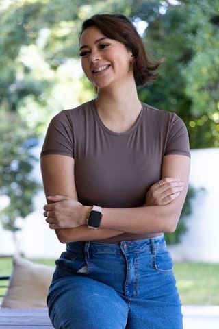 African american woman smiling with crossed arms wearing smartwatch and casual tee in backyard