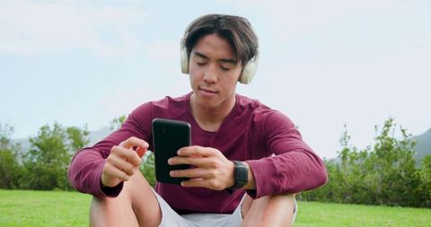 Young Man Sitting in Park Using Smartphone with Headphones