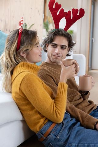 Festive couple relaxing with warm drinks and antler headbands