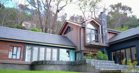 Contemporary wooden-clad hillside home with cantilevered balcony and stone chimney