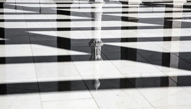 Reflecting ornate mosque columns through lattice shadows on polished marble floor