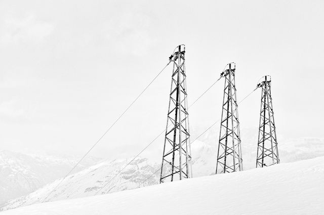 Snow-covered landscape featuring three ski lift towers amidst a mountainous backdrop. Ideal for depicting winter sports, travel, tourism, and nature-themed promotions. The minimalistic and serene setting is also suitable for advertisements related to outdoor activities in winter.