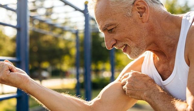 Mature man inspecting flexed bicep during outdoor calisthenics workout on blue bars