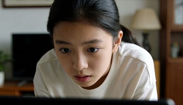 Teenage girl leaning toward laptop concentrating on screen in cozy living room closeup
