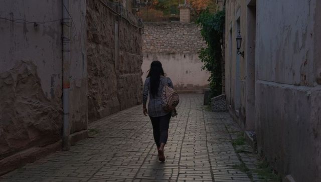 Woman walking through moody historic cobblestone alley carrying patterned shoulder bag