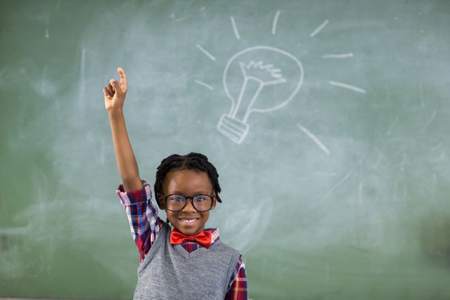 Young schoolboy with glasses raising his hand in a classroom, standing against a chalkboard with a lightbulb drawing. Ideal for educational content, school promotions, back-to-school campaigns, or illustrating concepts of learning and knowledge.