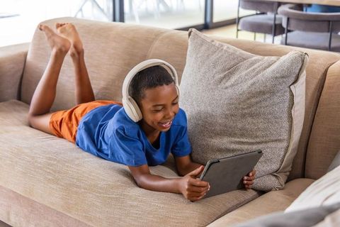 Boy wearing headphones lying on couch using tablet for learning and entertainment