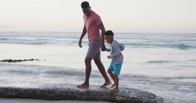 African american father walking with son on sunny beach. healthy and active time beach holiday.