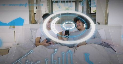 Laughing friends using smartphones and gamepad on bed with holographic HUD in cozy bedroom
