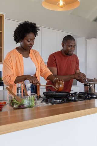 African american couple cooking together at kitchen island pouring sauce and stirring pot