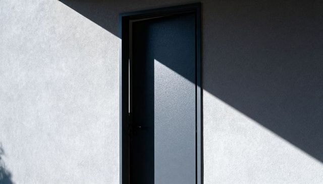 Minimalist steel entry door with bold diagonal sun shadow on smooth stucco wall