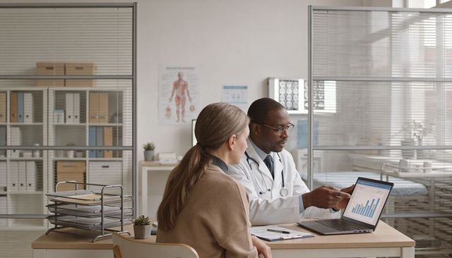 Doctor explaining medical data on laptop with bar chart to patient during clinic consultation