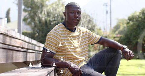 Young man sitting on bench checking watch with social network overlay in sunlit park