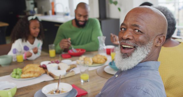 Image of happy african american grandfather turning and smiling at family breakfast table. Family, domestic life and togetherness concept digitally generated image.