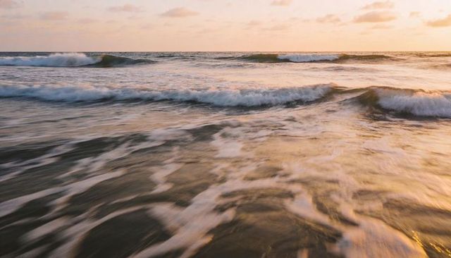 Golden sunset surf rolling over shallow shore, sea foam reflecting warm light