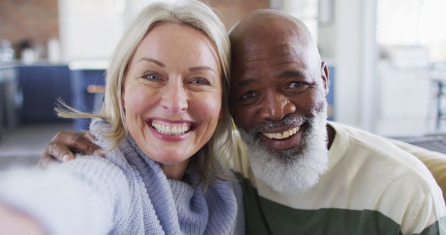 A cheerful senior couple smiling together in their cozy home, showcasing love and happiness in their retirement years. Ideal for advertisements promoting senior living, retirement communities, healthcare services, or lifestyle blogs focusing on relationships and diversity.