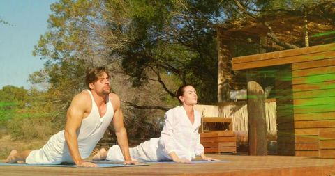 Couple practicing upward dog on sunlit wooden deck at tranquil outdoor yoga retreat