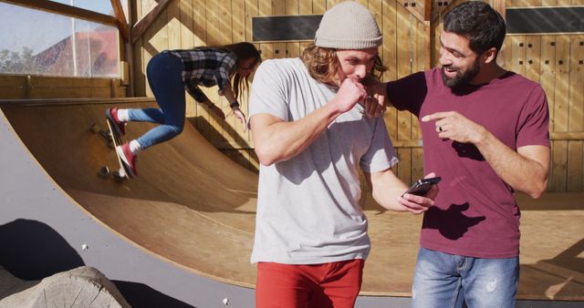 Image of happy diverse male skateboarders using smartphone in skate park. Skateboarding, sport, active lifestyle and hobby concept.