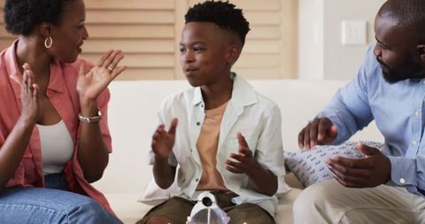 African American family celebrating birthday with young boy clapping on sofa
